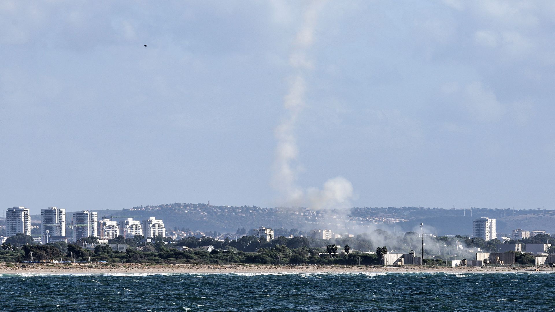 A plume of smoke billows after missiles were fired from Israel's Iron Dome missile-defence system batteries (R) to intercept rockets over the northern city of Acre on October 1, 2024.