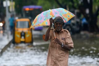 A man wades through a waterlogged road under an umbrella amid rain in Chennai