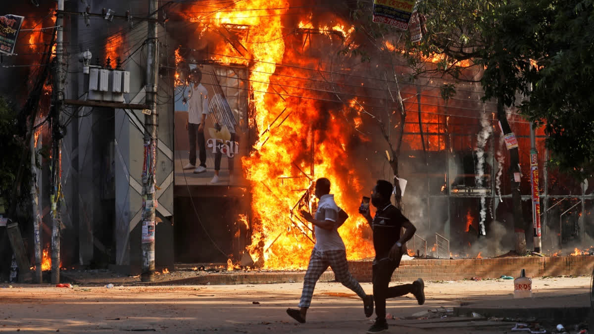 Men run past a shopping center which was set on fire by protesters during a rally against Prime Minister Sheikh Hasina and her government demanding justice for the victims killed in the recent countrywide deadly clashes, in Dhaka, Bangladesh, Sunday, Aug. 4, 2024.