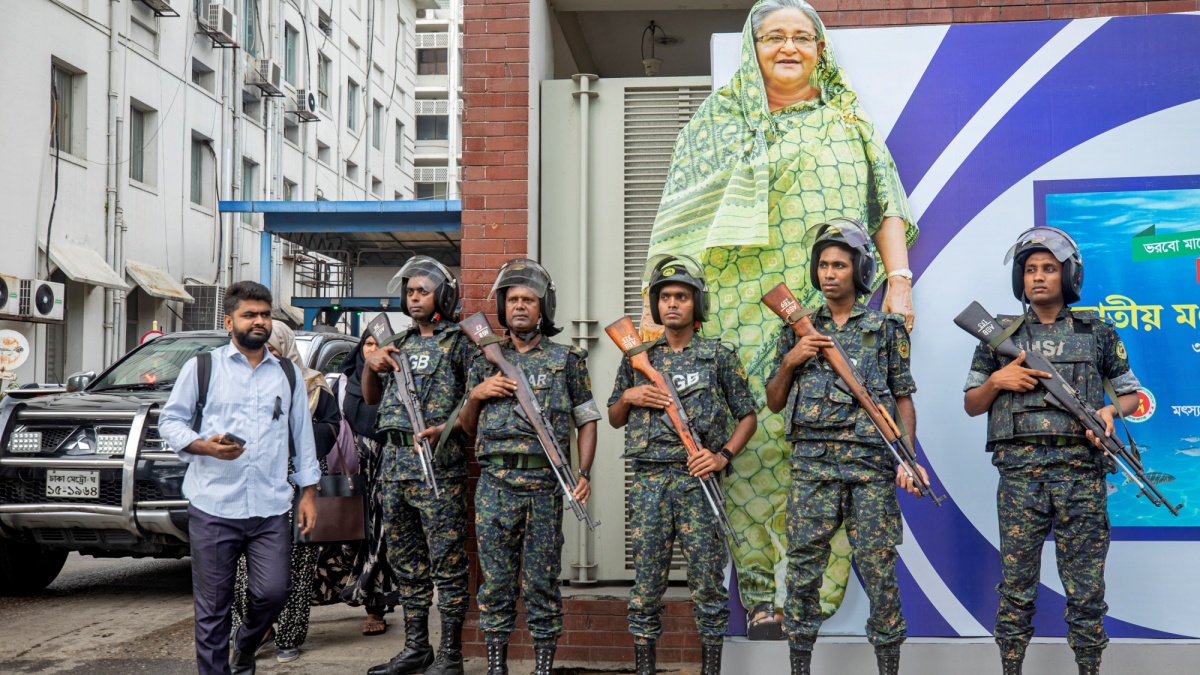 Security personnel stand guard in front of a large cutout portrait of now ousted Prime Minister Sheikh Hasina in Dhaka on July 30, 2024.