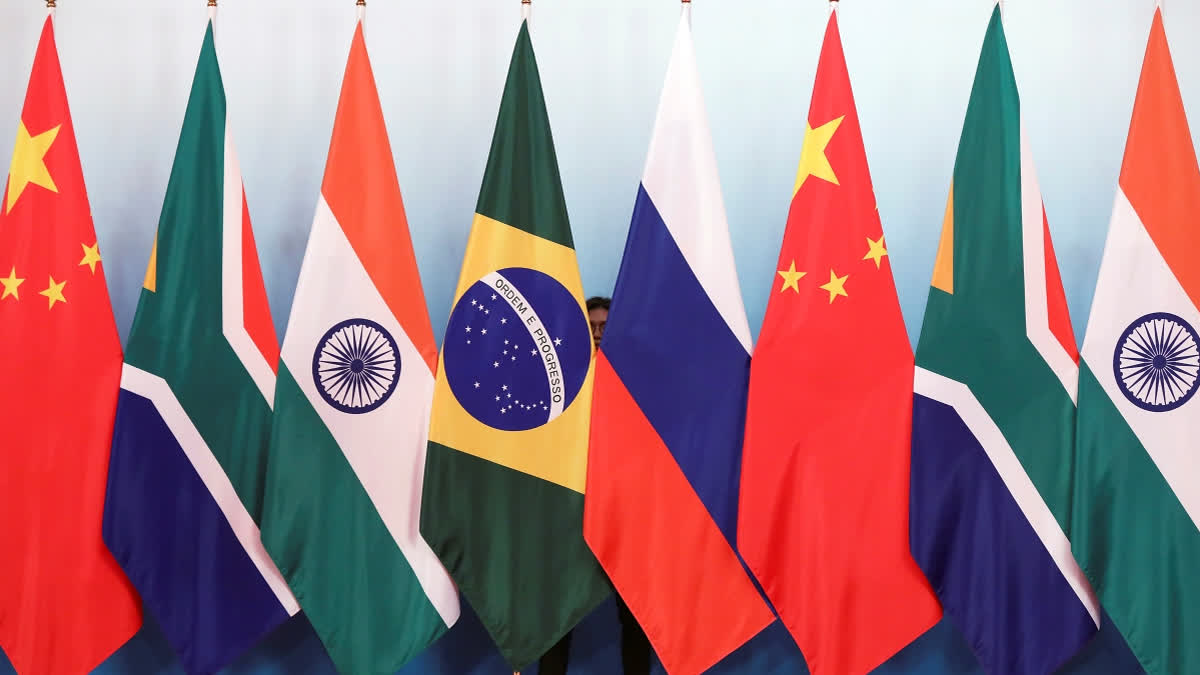 FILE - Staff worker stands behinds national flags of Brazil, Russia, China, South Africa and India to tidy the flags ahead of a group photo during the BRICS Summit at the Xiamen International Conference and Exhibition Center in Xiamen, southeastern China's Fujian Province, Monday, Sept. 4, 2017.