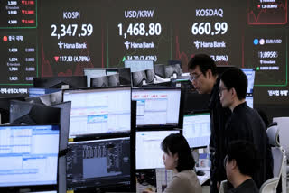 Currency traders watch monitors near a screen showing the Korea Composite Stock Price Index (KOSPI), top left, and the foreign exchange rate between U.S. dollar and South Korean won, top center, at the foreign exchange dealing room of the KEB Hana Bank headquarters in Seoul, South Korea, Monday, April 7, 2025.