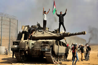 Palestinians wave their national flag and celebrate by a destroyed Israeli tank at the Gaza Strip fence east of Khan Younis southern Saturday, Oct. 7, 2023. The militant Hamas rulers of the Gaza Strip carried out an unprecedented, multi-front attack on Israel at daybreak Saturday, firing thousands of rockets as dozens of Hamas fighters infiltrated the heavily fortified border in several locations by air, land, and sea and catching the country off-guard on a major holiday. (AP Photo)