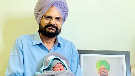 Late rapper Sidhu Moosewala's father poses for a photograph with his newborn son Shubhdeep with Moosewala's portrait in the background in March, 2024