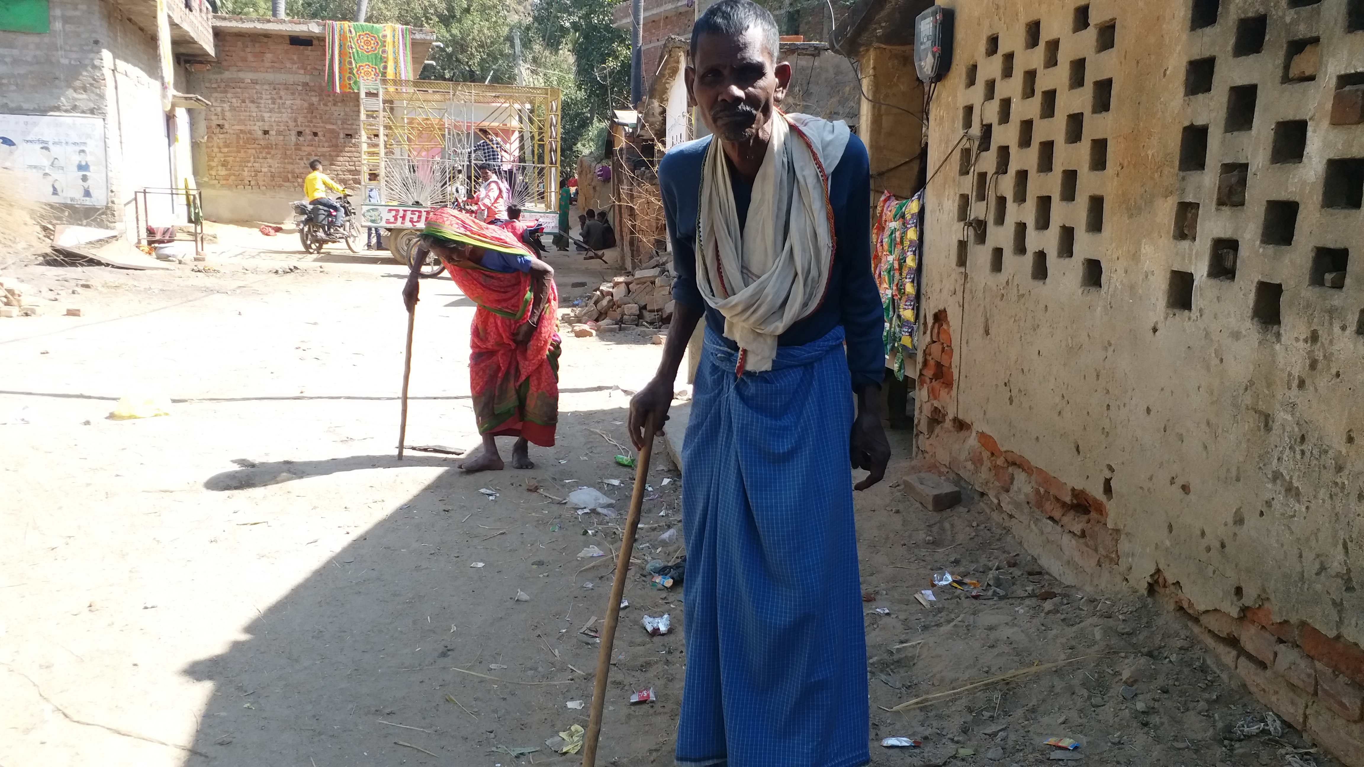 Two villagers walk with the support of sticks.