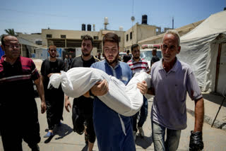 A Palestinian man holds the body of a child killed in the Israeli bombardment of the Gaza Strip, at a hospital morgue in Deir al-Balah, Tuesday, July 9, 2024.