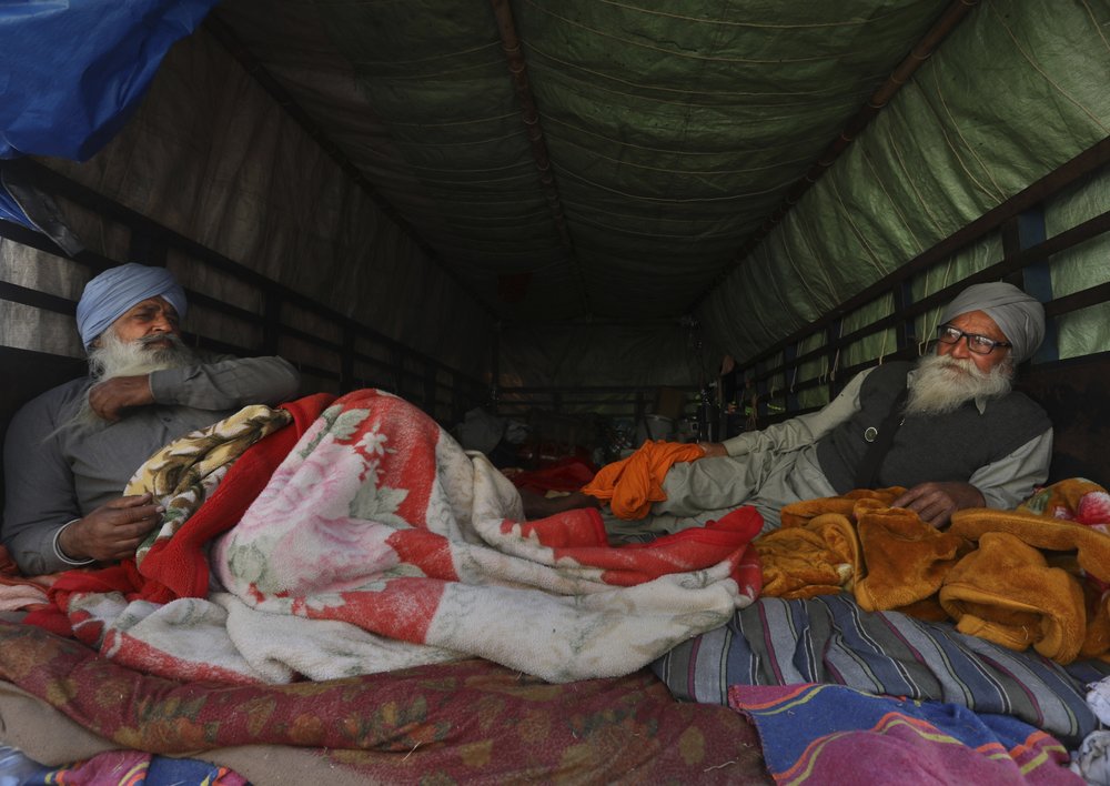 Protesting farmers sit at the back of their tractor trailer as they block a highway at the Delhi- Uttar Pradesh border