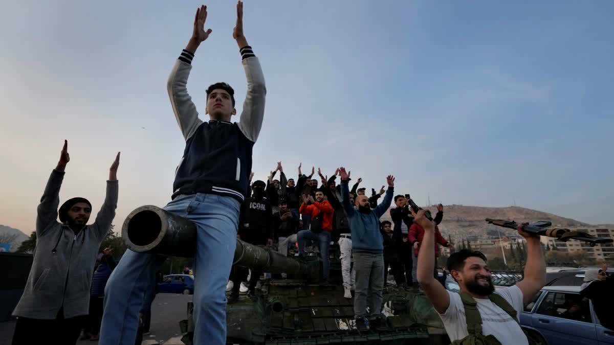 Syrian citizens stand on a government forces tank