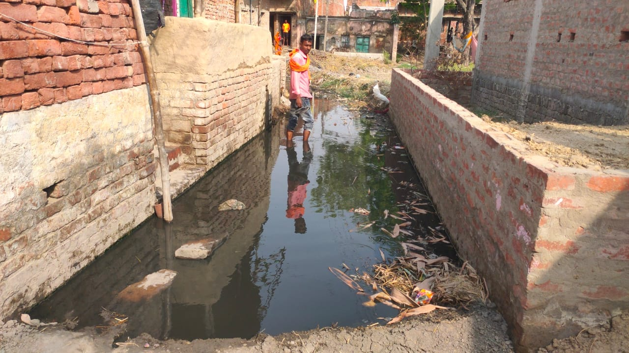 गली में जमा गंदे पानी में आते लोग