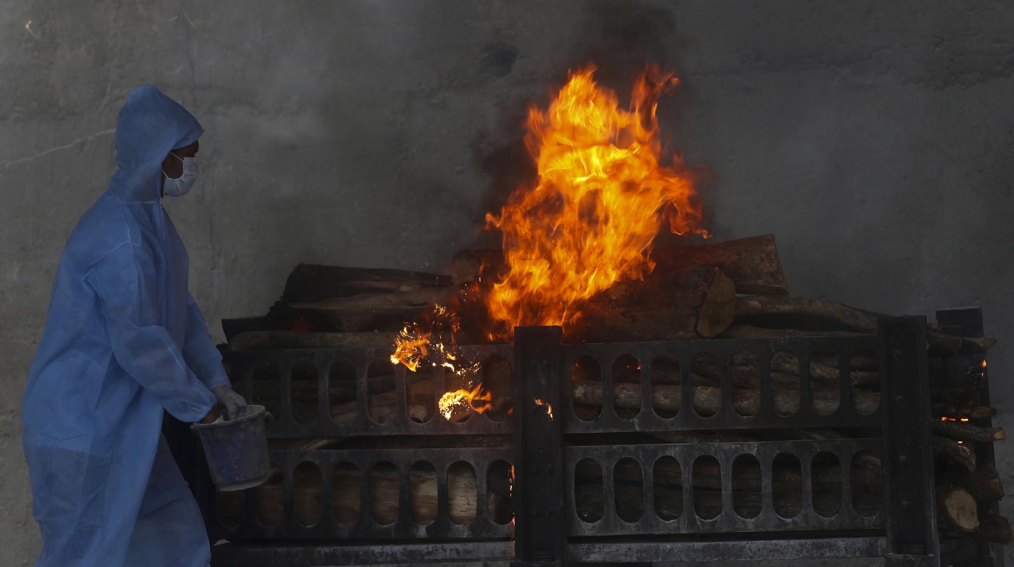 A municipal worker in personal protective suit performs last rites during the cremation of a COVID-19 victim in Vasai, on the outskirts of Mumbai