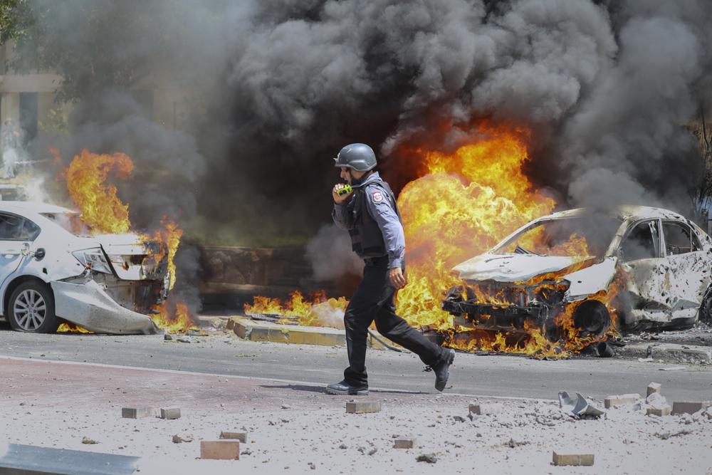 An Israeli firefighter walks next to cars hit by a missile fired from Gaza Strip, in the southern Israeli town of Ashkelon