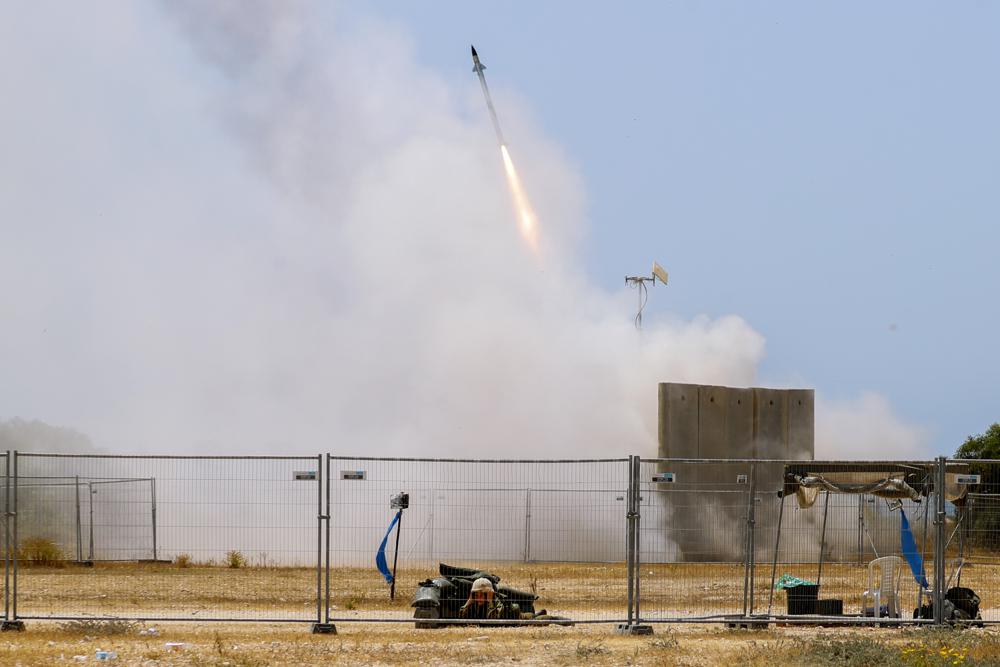 A Israeli soldier takes cover as an Iron Dome air defense system launches to intercept a rocket from the Gaza Strip, in Ashkelon