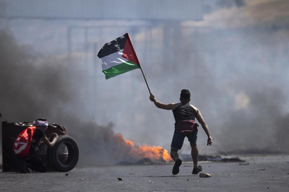 A protester waves the Palestinian flag during clashes with the Israeli forces at the Hawara checkpoint, south of the West Bank city of Nablus