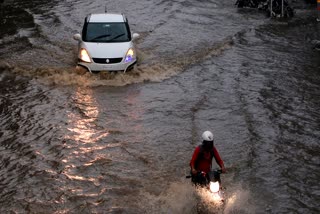 Commuters drive through a flooded road amid a heavy rain shower, in Ajmer