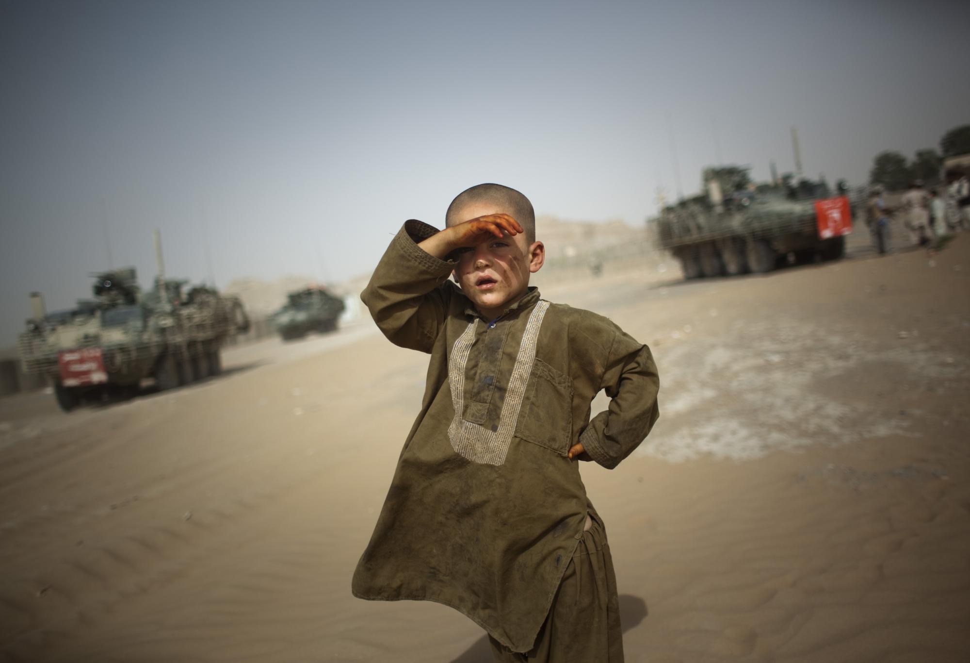 In this Aug. 6, 2009 file photo, a child watches military vehicles of 5th Striker Brigades drive past his village on the outskirts of Spin Boldak, about 100 kilometers (63 miles) southeast of Kandahar, Afghanistan.