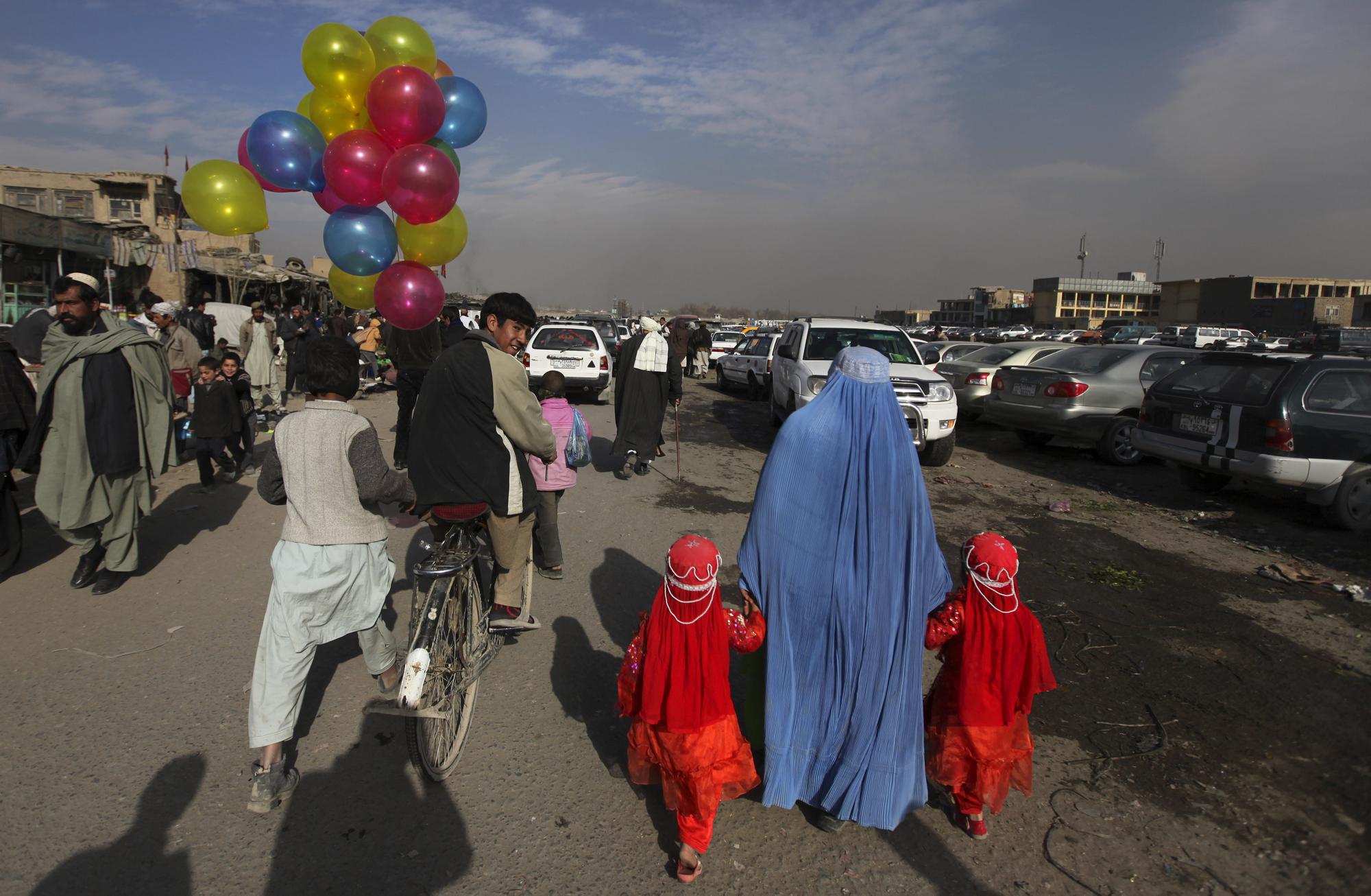A balloon seller riding a bicycle looks towards a woman holding hands with two young girls, Jan. 3, 2011, at a market in Kabul, Afghanistan.