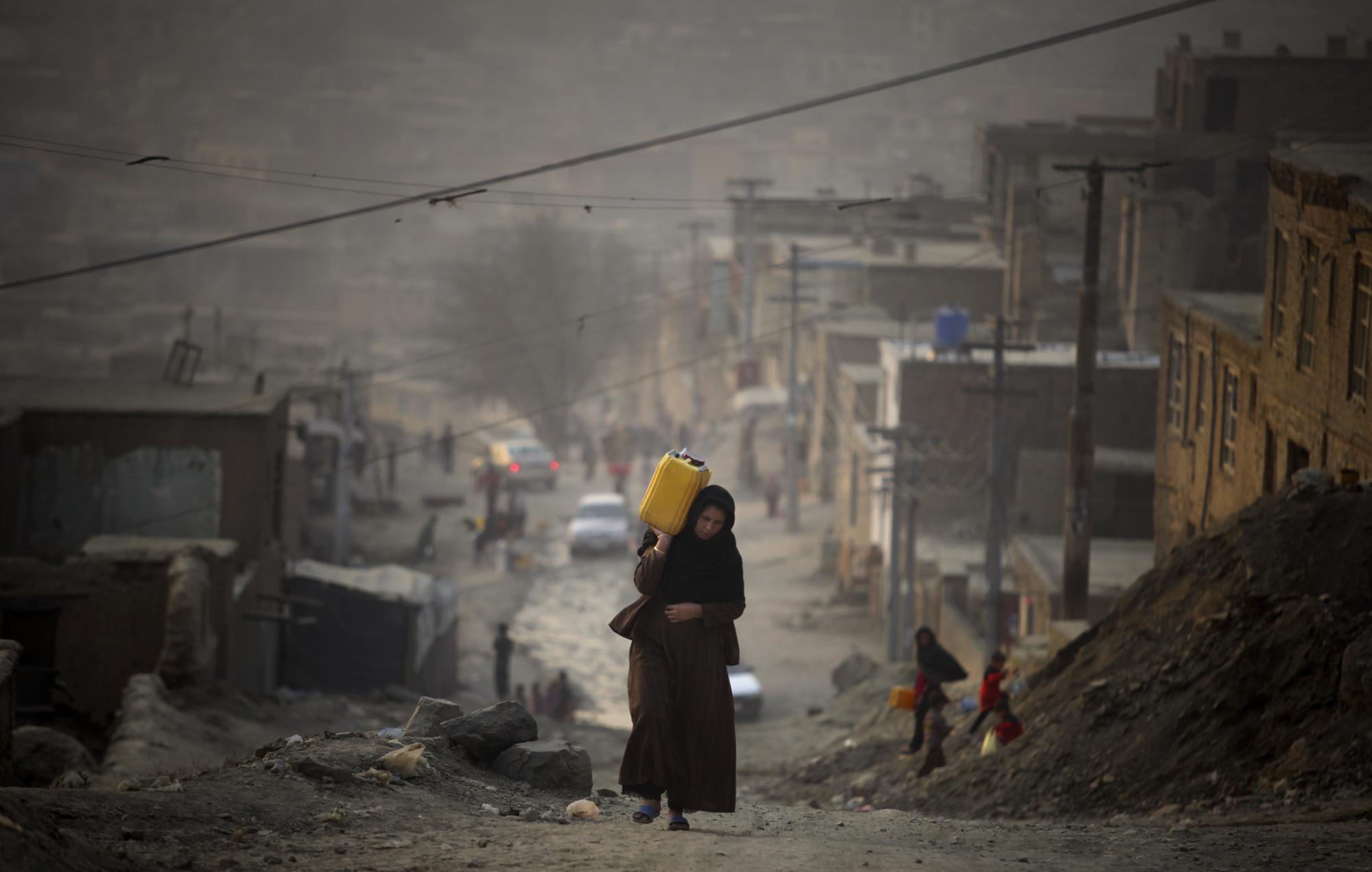 A woman carries water in a plastic container as she ascends a slope on the way towards her home, Dec. 27, 2010, in Kabul, Afghanistan.