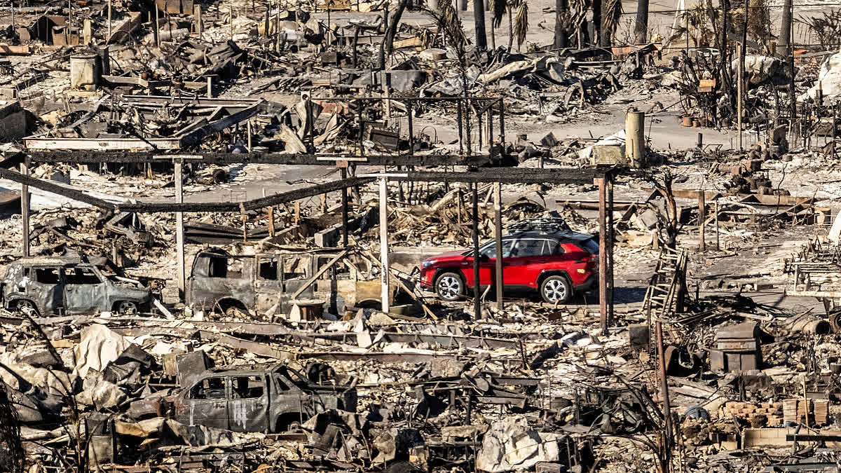 A car drives past homes and vehicles destroyed by the Palisades Fire at the Pacific Palisades Bowl Mobile Estates on Sunday, Jan. 12, 2025, in Los Angeles