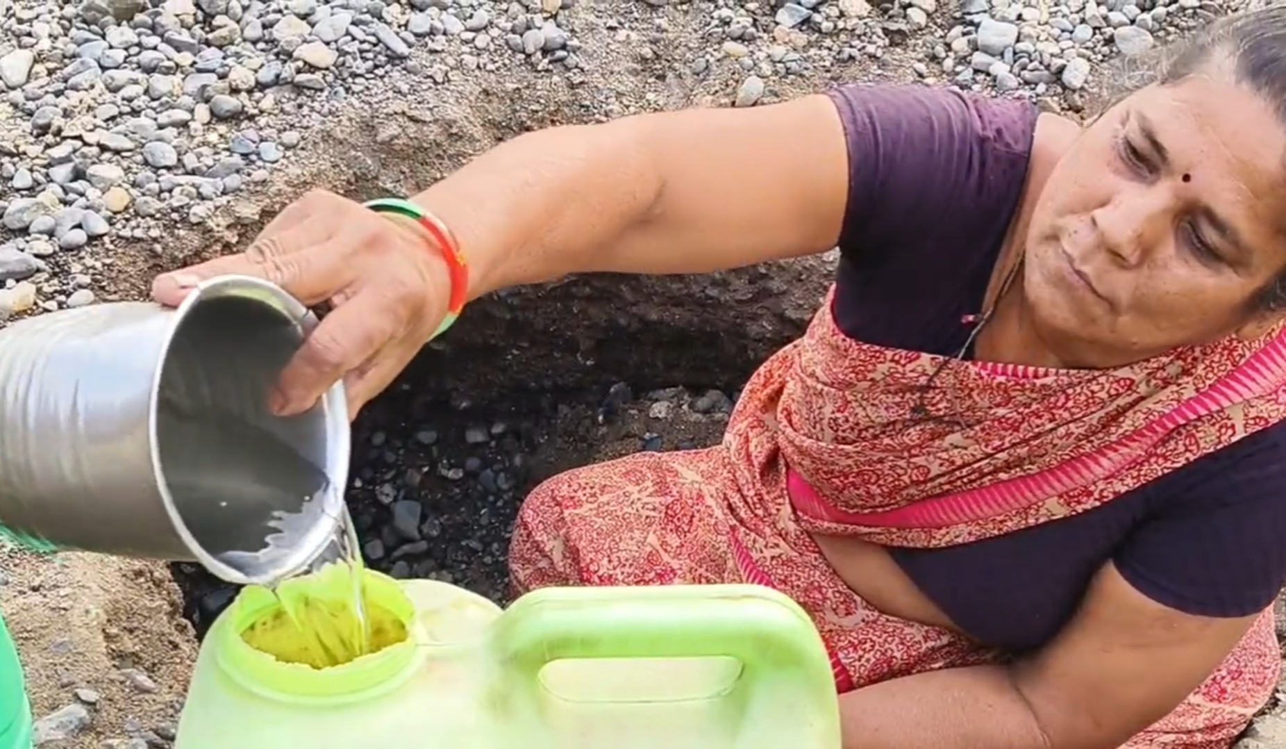 नदीत खड्डा खणून पाणी भरताना एक महिला