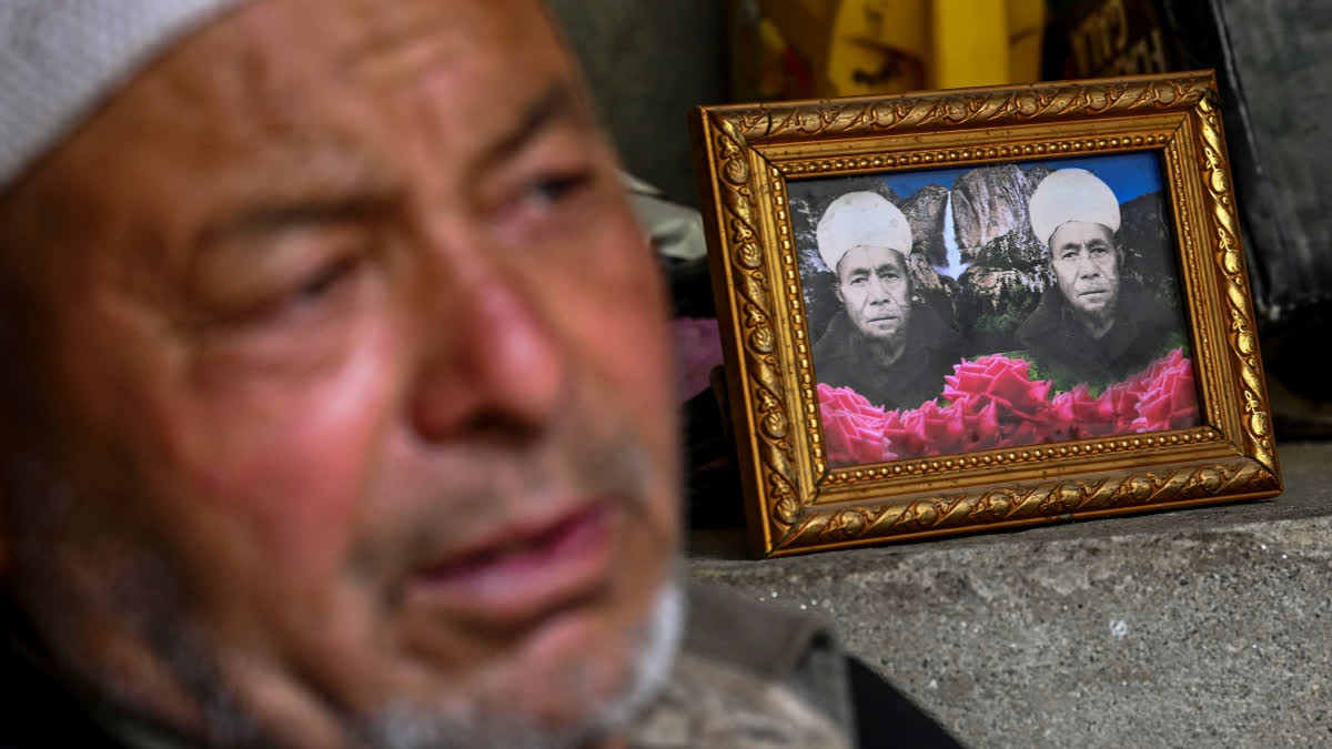 In this photograph taken on July 28, 2024 Ghulam Ahmad, an Indian apricot farmer sits beside a portrait of his father who died in Pakistan, as he speaks during an interview with AFP near Line of Control (LOC) - the border between India and Pakistan, at the Hunderman village in Kargil district.