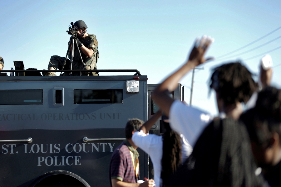 In this Wednesday, Aug. 13, 2014 file photo, a member of the St. Louis County Police Department points his weapon in the direction of a group of protesters in Ferguson, Mo. On Saturday, Aug. 9, 2014, a white police officer fatally shot Michael Brown, a Black teenager, in the St. Louis suburb.