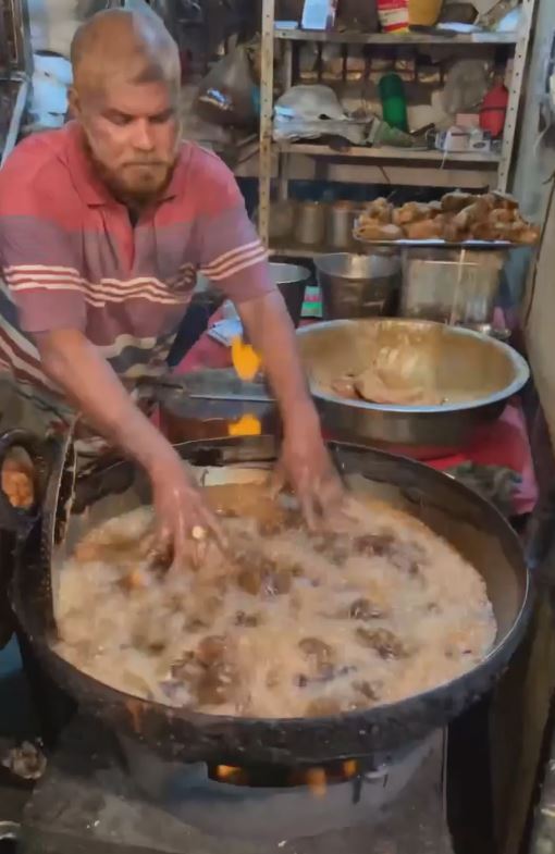 man dips his hand in boiling hot oil while making fried chicken