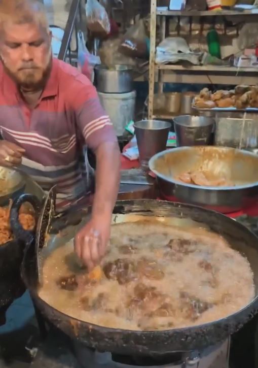 man dips his hand in boiling hot oil while making fried chicken