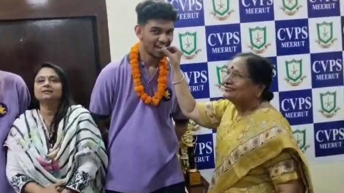 मेरठ के करण पिलानिया को मिठाई खिलातीं स्कूल की प्रिंसिपल.