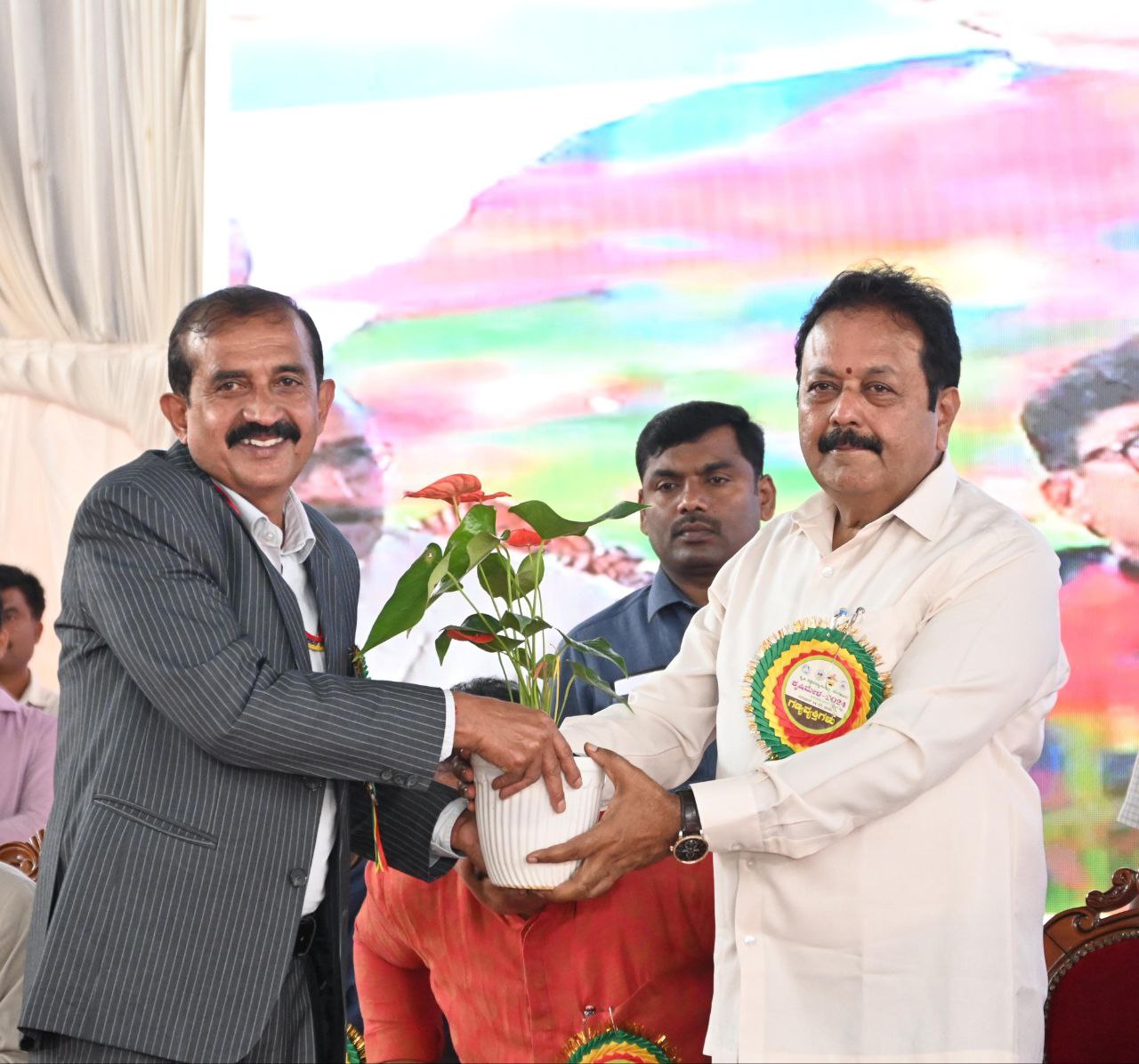 Karnataka Agriculture Minister N. Chaluvarayaswamy (R) presents a flower plant to an official at the Bengaluru Krishi Mela 2024