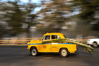 This photograph taken on January 28, 2025 shows passengers carrying banana and sugarcane trunks as they ride a Hindustan Ambassador yellow taxi, along a street in Kolkata.