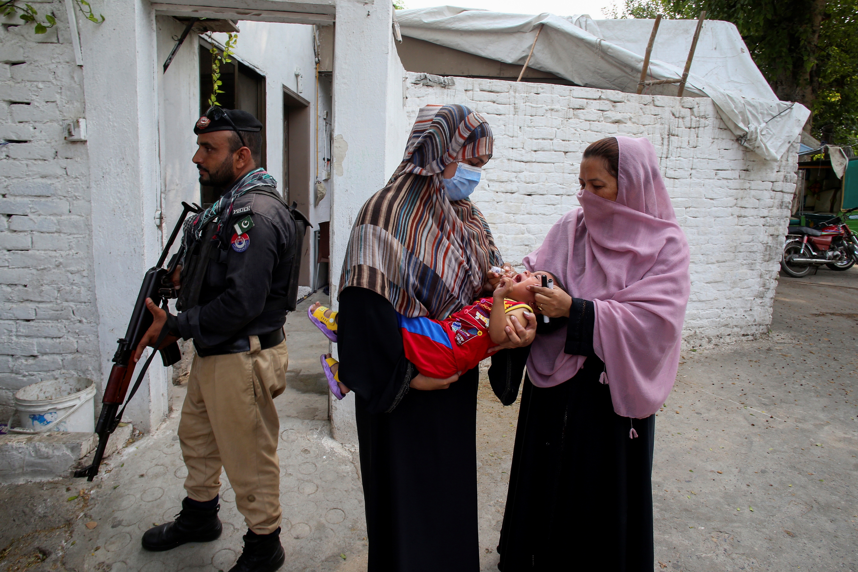 A police officer stands guard as a health worker, right, administers a polio vaccine to a child in a neighbourhood of Peshawar, Pakistan, Monday, Sept. 9, 2024.