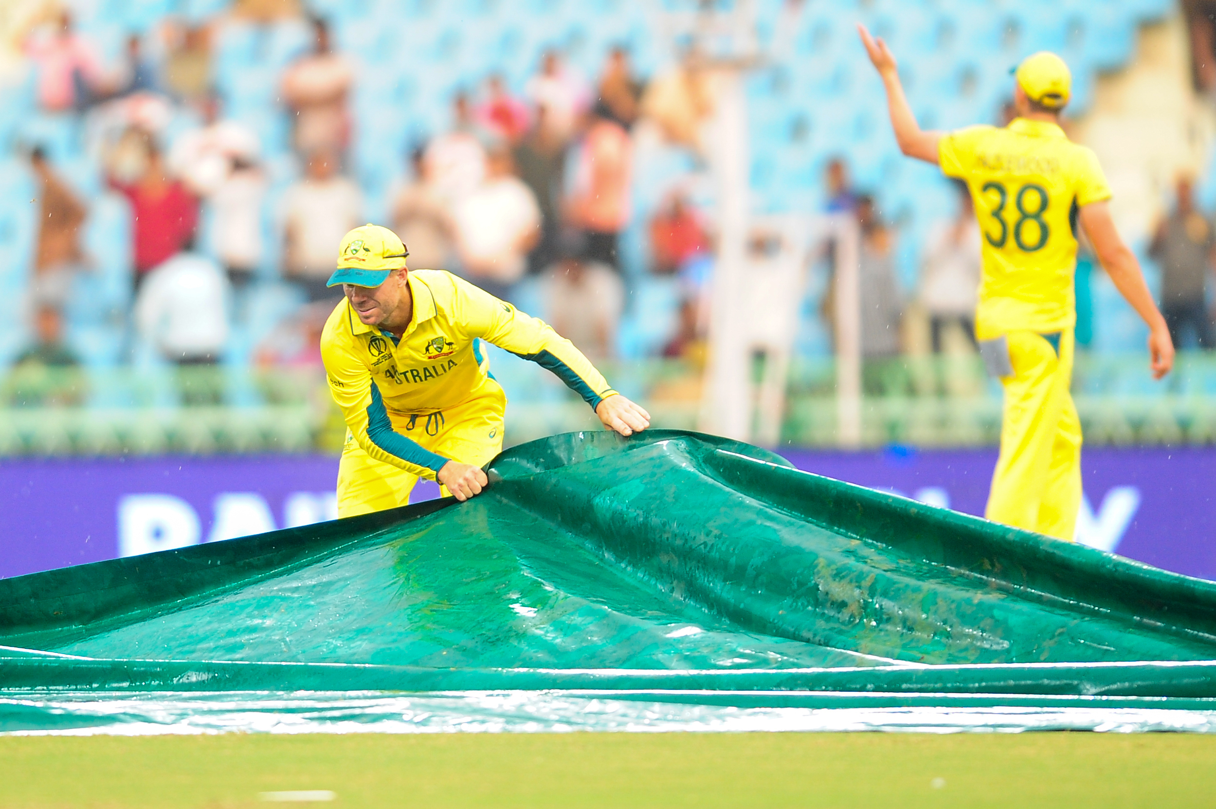 ICC Cricket World Cup  David Warner helps to groundsman  covers the field as rain disrupts the match  ಆಸ್ಟ್ರೇಲಿಯಾ ಶ್ರೀಲಂಕಾ ಪಂದ್ಯಕ್ಕೆ ವರುಣ ಅಡ್ಡಿ  ಗ್ರೌಂಡ್ಸ್​ಮನ್​ಗೆ​ ಸಹಾಯ ಮಾಡಿದ ವಾರ್ನರ್  ವಾರ್ನರ್​ಗೆ ಪ್ರಶಂಸೆಯ ಸುರಿಮಳೆ  ಏಕಾನಾ ಕ್ರಿಕೆಟ್ ಸ್ಟೇಡಿಯಂ  ಆಸ್ಟ್ರೇಲಿಯಾ ಮತ್ತು ಶ್ರೀಲಂಕಾ ನಡುವಿನ ಪಂದ್ಯ  ಆಸ್ಟ್ರೇಲಿಯಾದ ಡೇವಿಡ್ ವಾರ್ನರ್ ಗ್ರೌಂಡ್ಸ್​ಮನ್  ಕ್ರಿಕೆಟ್ ವಿಶ್ವಕಪ್ 2023 ಪಂದ್ಯ  ಡೇವಿಡ್ ವಾರ್ನರ್ ಗ್ರೌಂಡ್ಸ್‌ಮನ್​ಗೆ ಸಹಾಯ  ಕೆಲ ಸಮಯ ಮಳೆ ಸುರಿಯಿತು