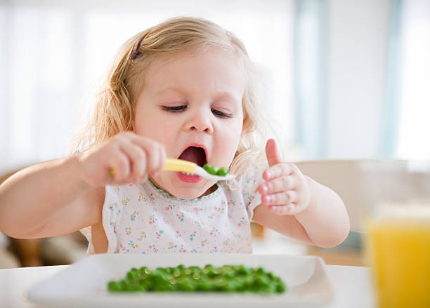 A girl eating peas with spoon