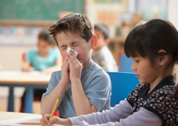 boy blowing nose in classroom