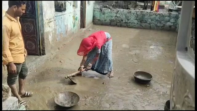 बिपरजॉय की बारिश के बाद जलमग्न घरों से मलबा निकालती महिला