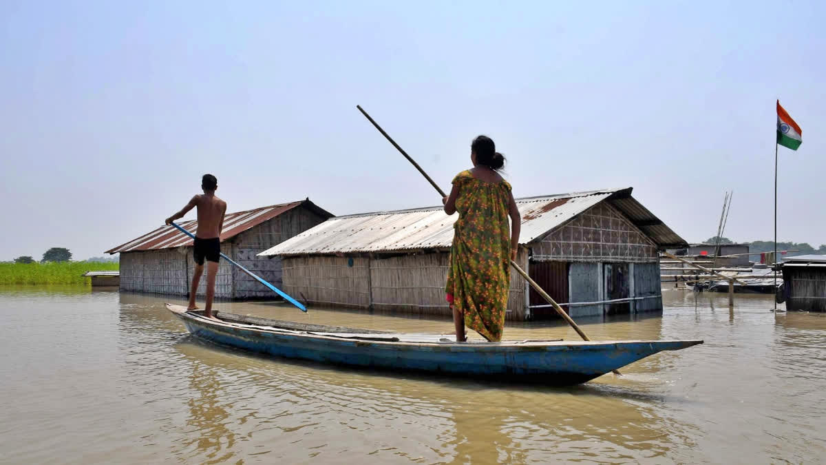 People paddle a boat near their partially submerged houses in the flood affected Hiloikhunda village in Morigaon district of Assam in 2023