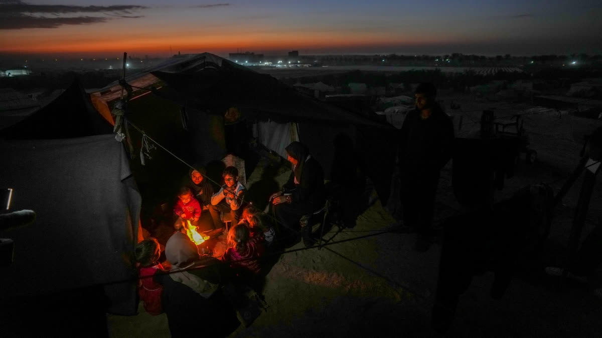 Reda Abu Zarada, 50, displaced from Jabaliya in nothern Gaza, sits by a fire with her grandchildren at a camp by the sea in Khan Younis, Gaza Strip, Thursday, Dec. 19, 2024.