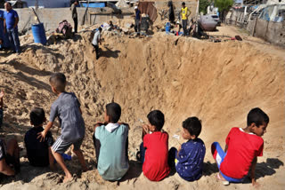 Palestinian children sit at the edge of a crater after an Israeli airstrike in Khan Younis, southern Gaza Strip, Friday, June 21, 2024.