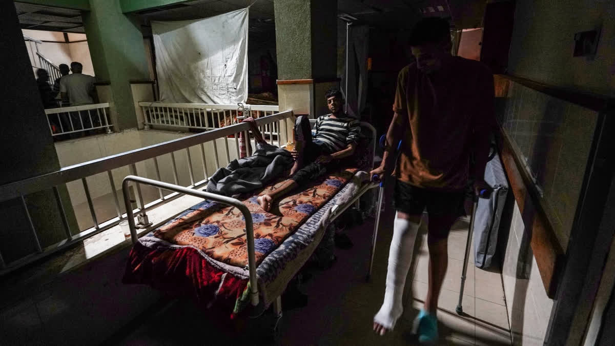 A patient lies in a bed as another walks by in a corridor lit by sunlight seeping through windows, after a partial power cut at the Al-Aqsa Martyrs Hospital in Deir al-Balah on May 23, 2024, amid continuing battles between Israel and Hamas in the Gaza Strip.