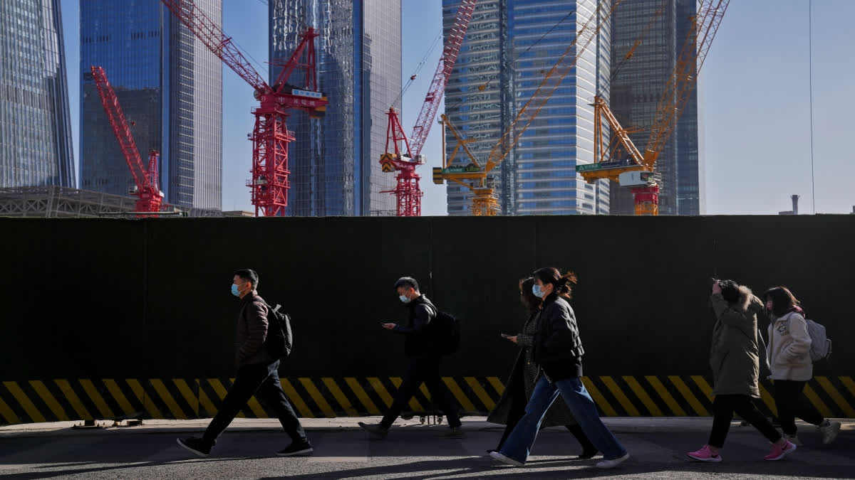 FILE - People wearing face masks walk by construction cranes near the office buildings at the central business district in Beijing, on March 15, 2023. China's leaders have mounted a campaign to build confidence in the slowing economy by freeing up billions of dollars in cash for property lending and other spending.