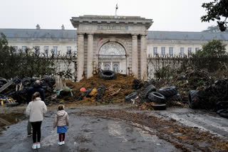 People watch slurry, manure and tyres dumped by farmers at the entrance of the local state administration building, in Agen, southwestern France, Saturday, Jan. 27, 2024. French farmers have vowed to continue protesting and are maintaining traffic barricades on some of the country's major roads. The government announced a series of measures Friday but the farmers say these do not fully address their demands. (AP Photo/Fred Scheiber)