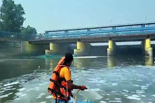 A Delhi Jal Board staff sprays chemicals into the Yamuna River to dissolve the toxic foam seen floating on the river, at Kalindi Kunj, in New Delhi