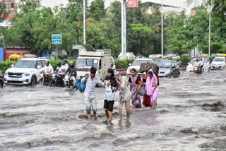 People walk through a heavily waterlogged road as vehicles pass by during heavy rainfall in Jaipur on Tuesday, July 08, 2025.