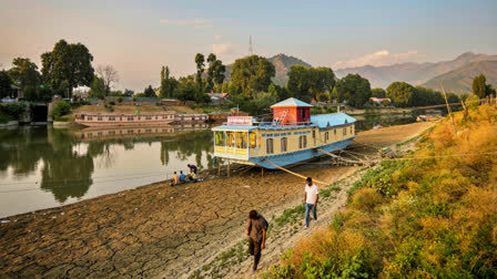 A house boat seen on the dried portion of the Jhelum river as people walk on a hot summer day in Srinagar, Kashmir on July 25, 2024.