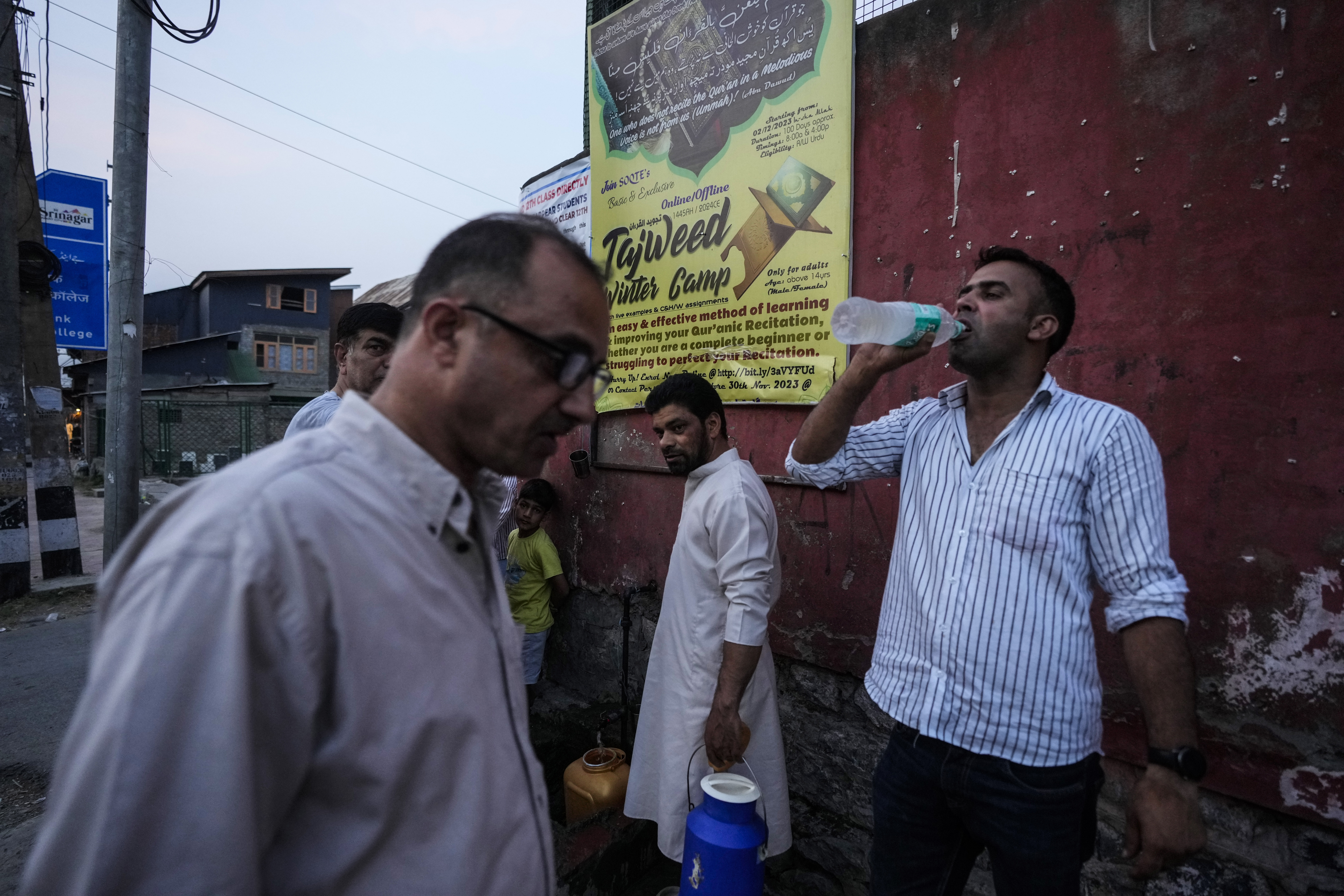 A Kashmiri man drinks water after collecting it from a public water tap as others wait for their turn on a hot summer evening in Srinagar, Kashmir, on July 28, 2024.