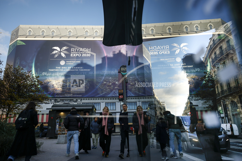 People walk by a building under renovation protected with a canvas decorated with a commercial promoting the Riyadh Expo 2030