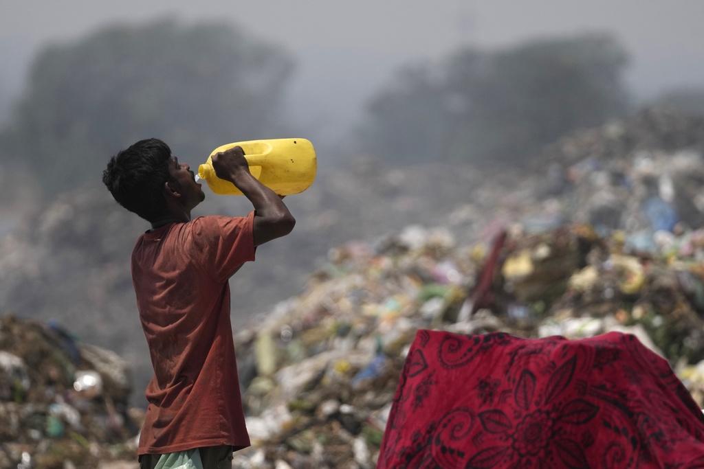 A waste picker drinks water while working during a heat wave at a garbage dump