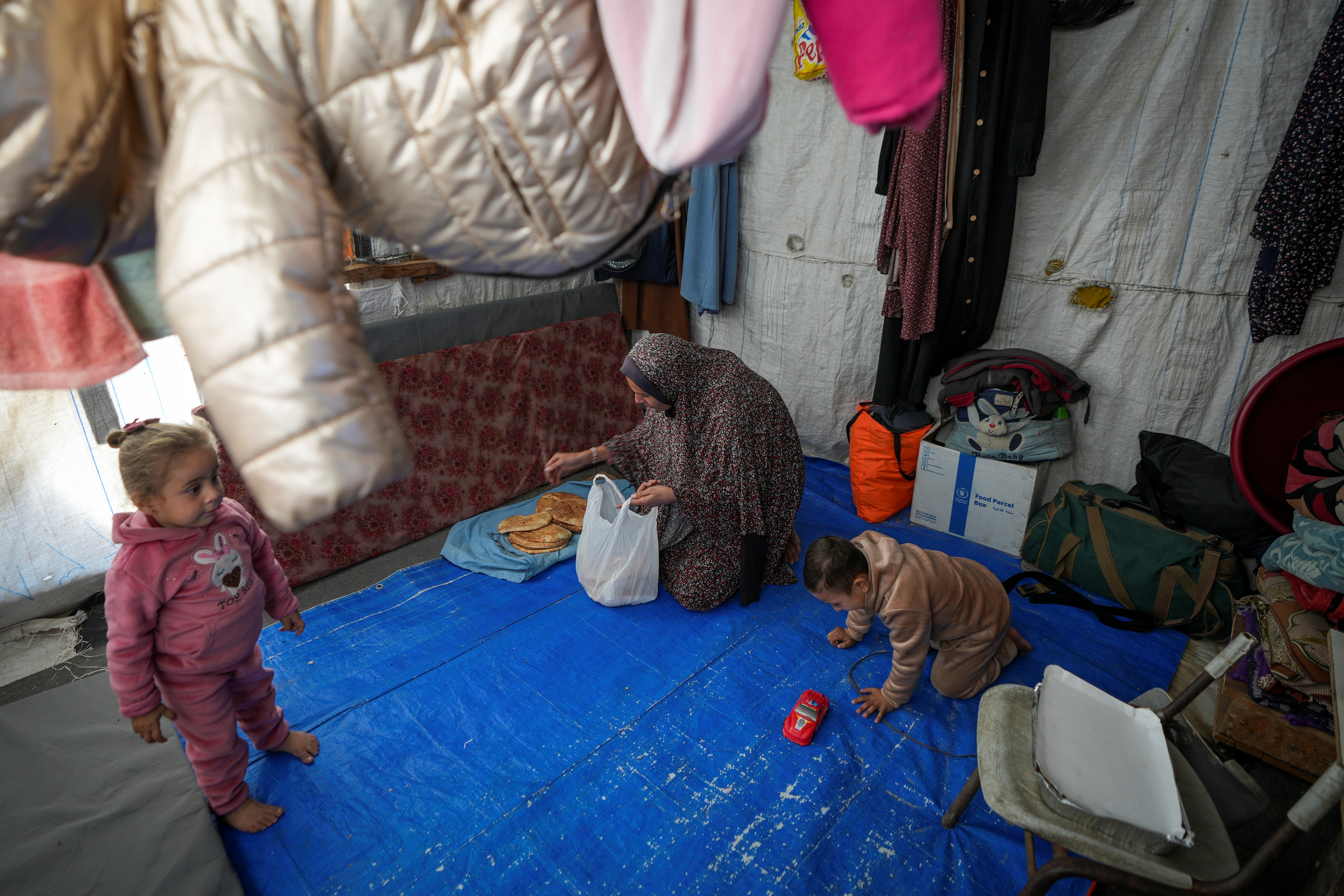 Wafaa Nasrallah places bread on a tray as her 4-year-old son, Ameer, plays nearby and her 2-year-old daughter, Ayloul, stands at their tent.