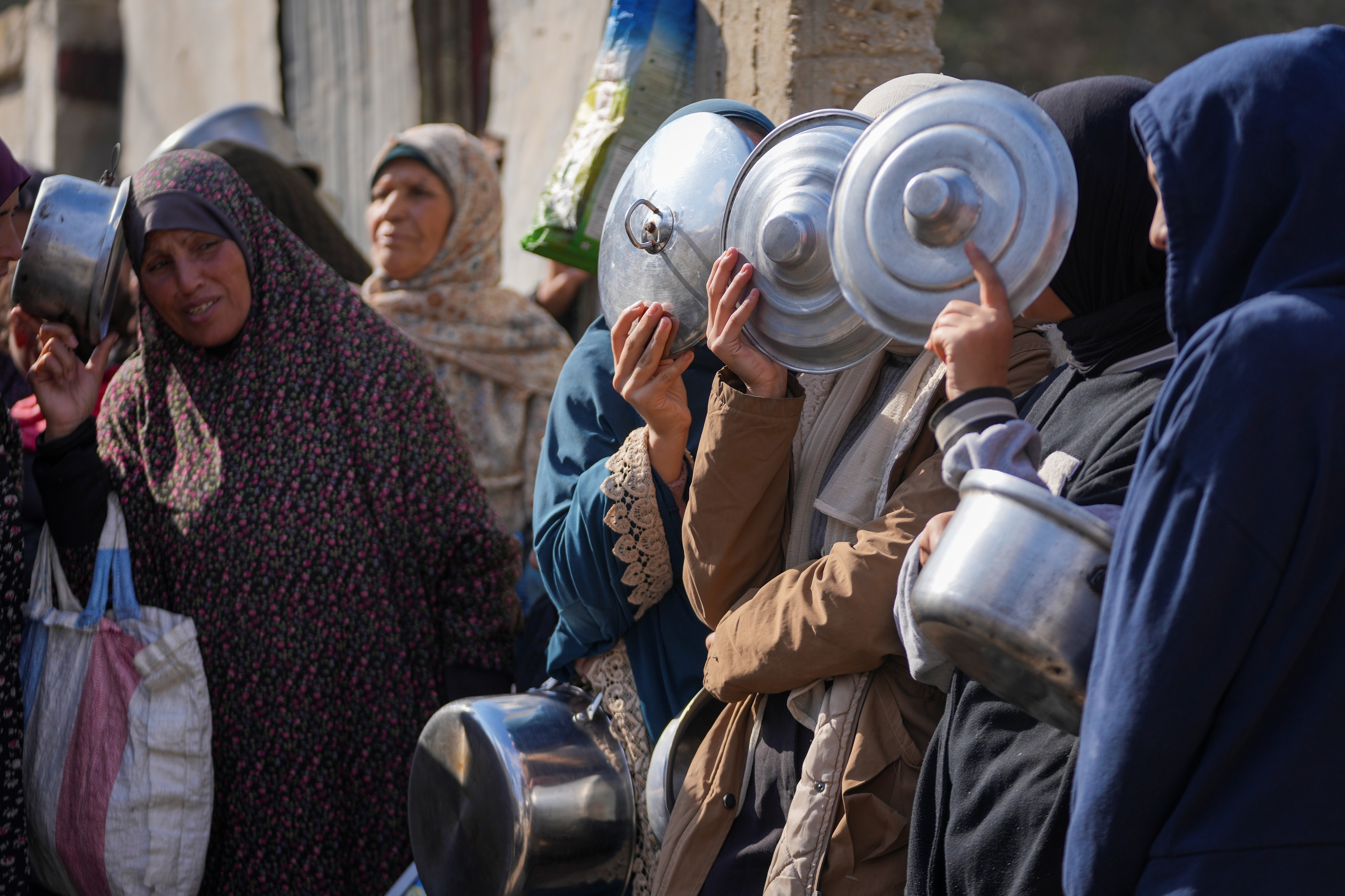 Women cover their faces as they line up to receive donated food at a distribution center for displaced Palestinians.