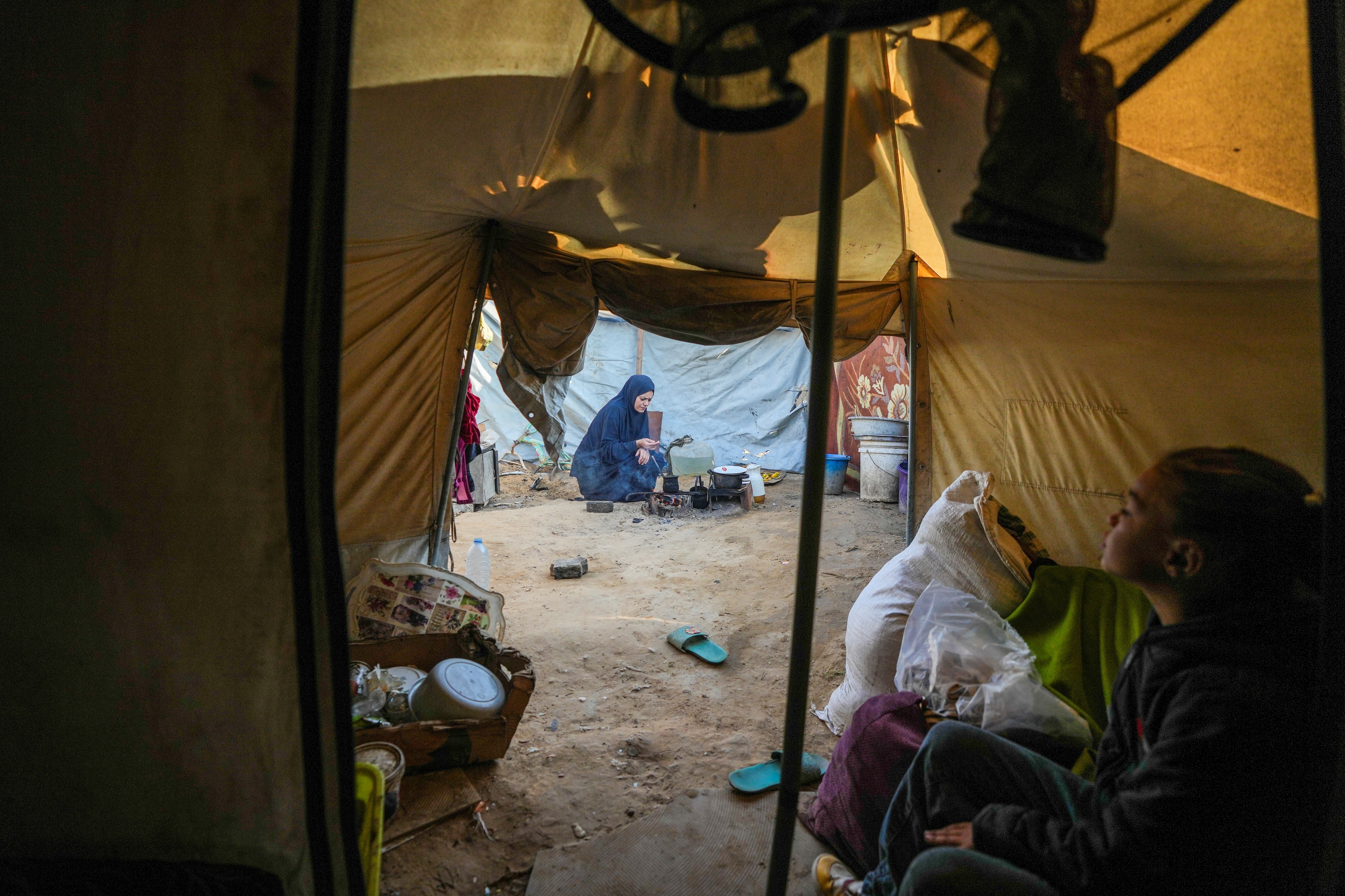 Alaa Hamami prepares a meal while her 10-year-old daughter, Basant, sits inside their tent at a camp.